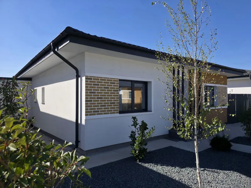 Casa Parter finalizată în Tunari — colțul casei, cu fereastra placată cu cărămidă, mesteacănul și grădina cu pietriș